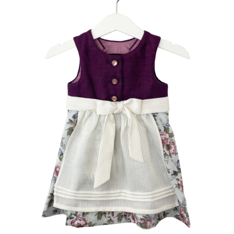 Babydirndl aus bordeaux-farbenen Leinenoberteil mit passepoilliertem Ausschnitt und 3 Knöpfe. Geblümter Rock mit Falten. Schürze ist einfärbig creme mit Bund und Bänder zum binden.