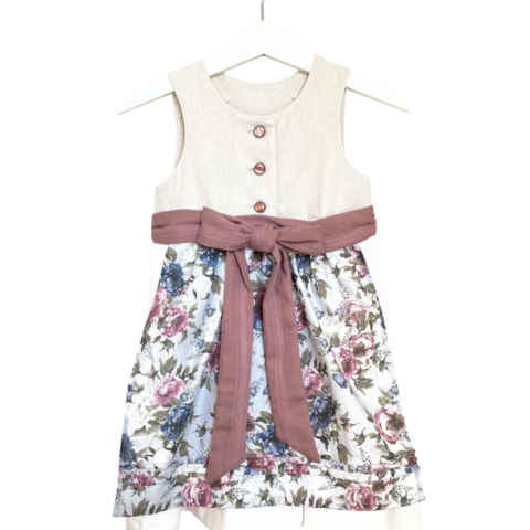 Babydirndl aus beigem Leinenoberteil mit passepoilliertem Ausschnitt und 3 Knöpfe. Creme-farbener Leinenrock mit Falten. Schürze ist geblümt mit einfärbigem Bund und Bänder zum binden.