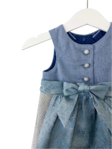 Babydirndl aus blauem Leinenoberteil mit passepoilliertem Ausschnitt und 3 Knöpfe. Gemusterter Leinenrock mit Falten. Schürze ist gemustert mit Bund und Bänder zum binden.