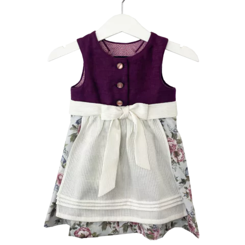 Babydirndl aus bordeaux-farbenen Leinenoberteil mit passepoilliertem Ausschnitt und 3 Knöpfe. Geblümter Rock mit Falten. Schürze ist einfärbig creme mit Bund und Bänder zum binden.