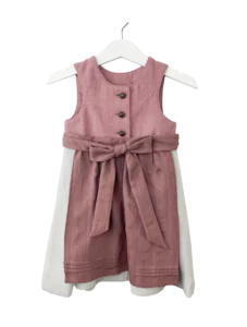 Babydirndl aus rosa-farbenen Leinenoberteil mit passepoilliertem Ausschnitt und 3 Knöpfe. Einfärbig beiger Rock mit Falten. Schürze ist einfärbig altrosa mit Bund und Bänder zum binden.