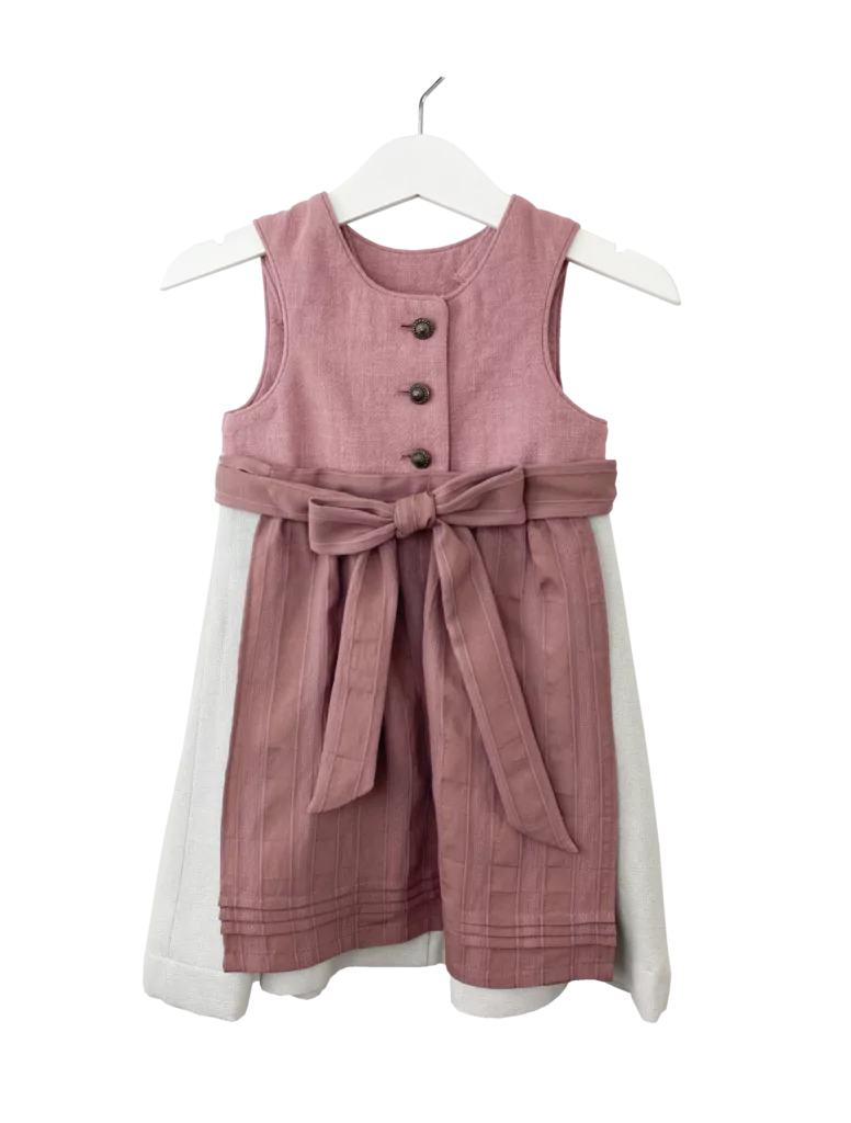 Babydirndl aus rosa-farbenen Leinenoberteil mit passepoilliertem Ausschnitt und 3 Knöpfe. Einfärbig beiger Rock mit Falten. Schürze ist einfärbig altrosa mit Bund und Bänder zum binden.